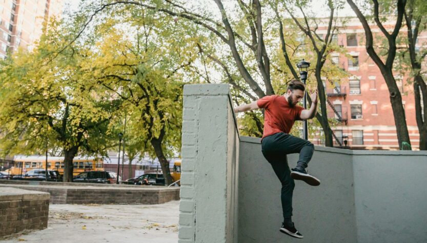 Full body side view of young man in sportswear performing parkour trick on while jumping off concrete border in street