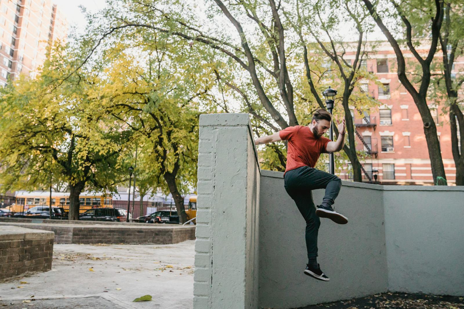 Full body side view of young man in sportswear performing parkour trick on while jumping off concrete border in street